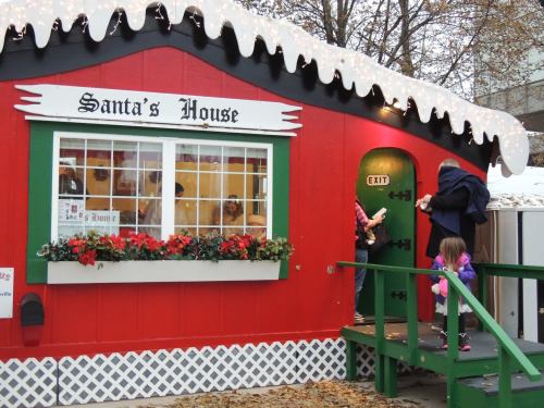 A colorful, festive cabin labeled "Santa's House" with holiday decorations and children visiting.