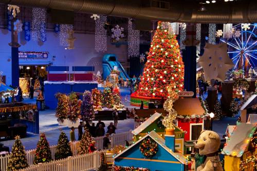 A festive indoor scene featuring a large decorated Christmas tree, colorful displays, and holiday decorations.