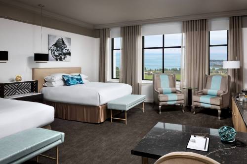 A modern hotel room featuring two beds, a seating area, large windows with a view, and stylish decor.