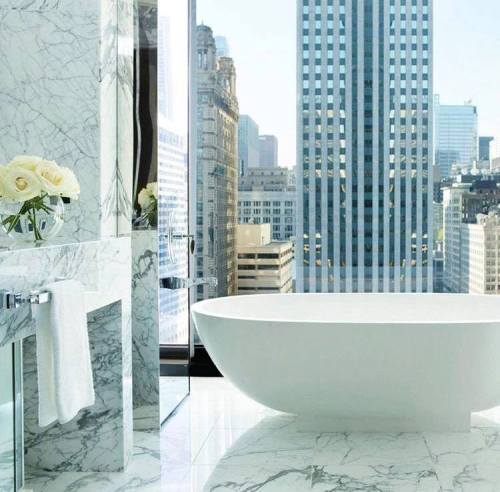 A modern bathroom with a freestanding tub, marble accents, and a large window showcasing a city skyline.