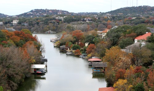 A serene river scene with autumn foliage, houses, and boat docks along the water's edge.