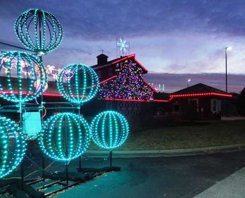 Colorful holiday lights adorn a building and decorations, set against a twilight sky.