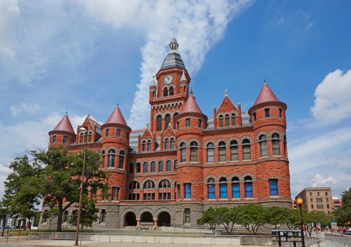 Historic red brick building with turrets and a clock tower, set against a blue sky with scattered clouds.