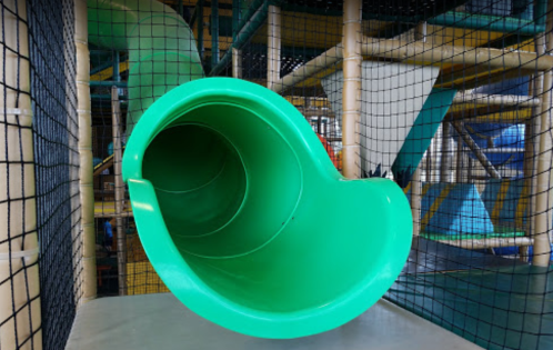A green slide inside a play structure, viewed from the entrance, with netting in the background.