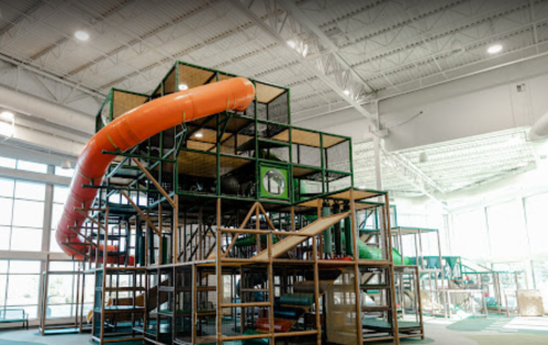 Indoor playground structure with multiple levels, slides, and an orange tube slide. Bright and spacious environment.