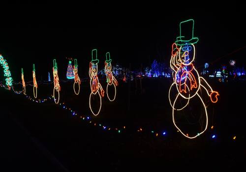A row of illuminated snowmen with green hats and colorful lights against a dark night sky.