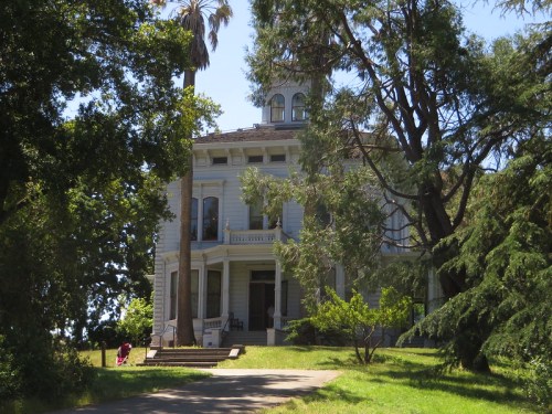 A large, historic white house surrounded by trees and greenery on a sunny day.