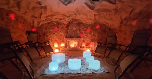 A serene salt cave with glowing salt lamps, comfortable chairs, and crystal bowls arranged on a rug.