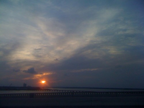 A sunset over a calm body of water, with clouds scattered across a colorful sky.