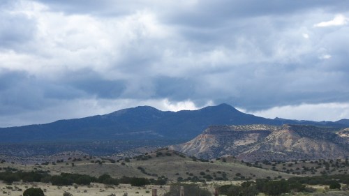 A scenic view of mountains under a cloudy sky, with rolling hills and sparse vegetation in the foreground.
