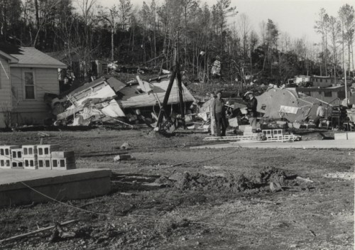 A man surveys a devastated area with destroyed buildings and debris after a natural disaster.