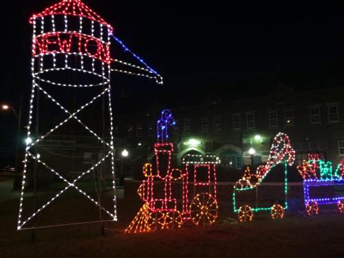 Colorful holiday lights depict a train and a water tower, creating a festive scene at night.