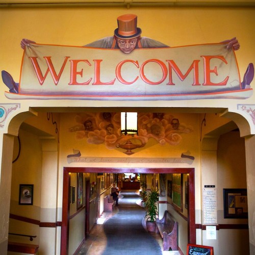 A colorful mural of a man in a top hat holding a "Welcome" banner in a hallway with art on the walls.