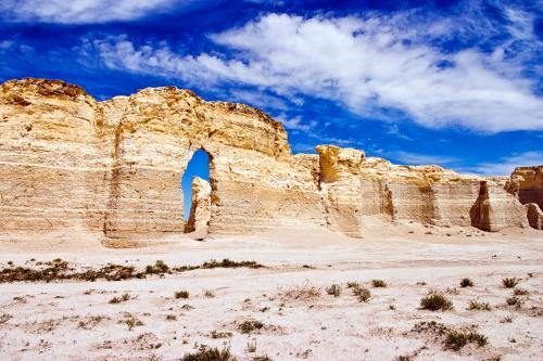 A rocky landscape featuring a large arch formation against a blue sky with scattered clouds.