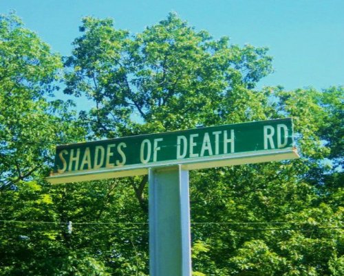 Sign for "Shades of Death Rd" surrounded by lush green trees.