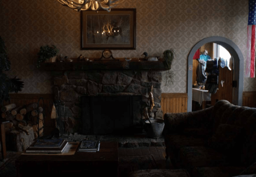 Cozy living room with a stone fireplace, wooden accents, and a glimpse of a dining area in the background.