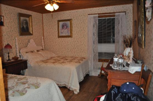 Cozy bedroom with two beds, floral wallpaper, vintage portraits, and a wooden dresser with glassware.