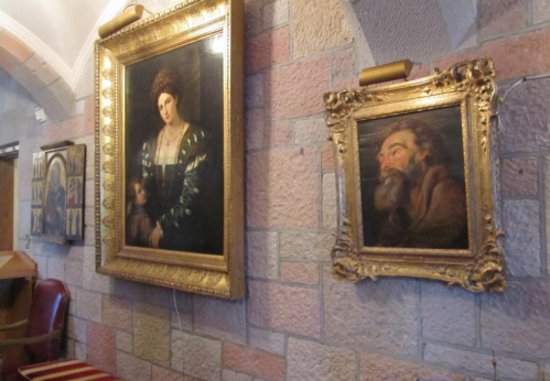 Two ornate framed paintings hang on a stone wall, featuring a woman and a man with a beard.