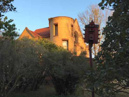 A historic brick building with a rounded turret, surrounded by trees and a red birdhouse in the foreground.