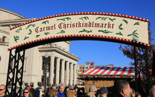 A festive archway reading "Carmel Christkindlmarkt" with a crowd and holiday market in the background.