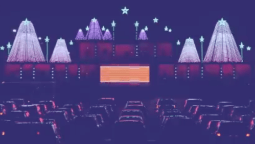 Colorful holiday lights decorate a drive-in theater, with illuminated trees and stars against a dark sky.