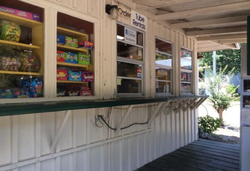 A small outdoor kiosk with windows displaying snacks and rental options, set in a rustic wooden structure.