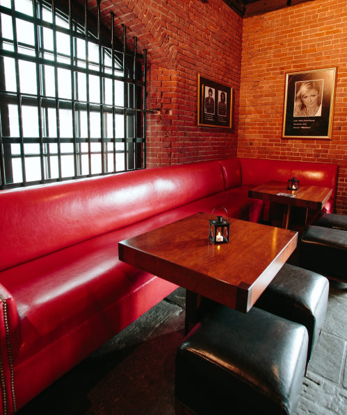 Cozy restaurant interior featuring a red leather booth, wooden tables, and brick walls with framed photos.