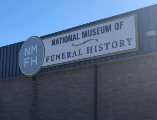 Sign for the National Museum of Funeral History, featuring the initials NMFH, against a clear blue sky.