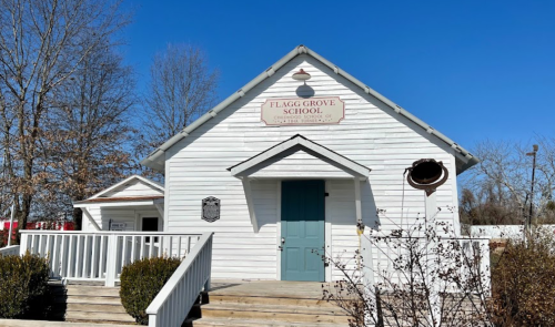 Historic Flagg Grove School building with a blue door, white exterior, and clear blue sky in the background.