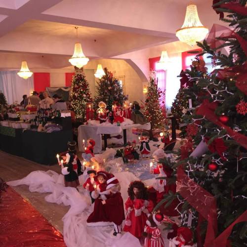 A festive room decorated with Christmas trees, dolls, and holiday decorations, creating a cheerful holiday atmosphere.