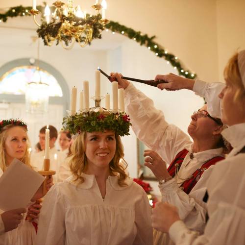 A group of people in white dresses celebrate with candles and a crown of lights, creating a festive atmosphere.