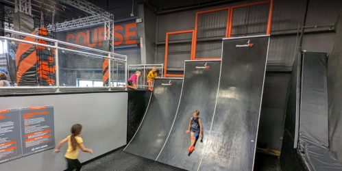 Children play on a climbing course with steep ramps in a brightly colored indoor facility.