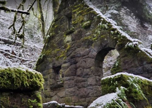 A moss-covered stone ruin surrounded by trees and snow, evoking a sense of mystery in a winter landscape.