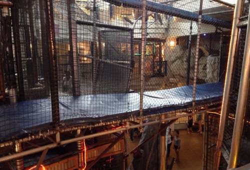 A view of a multi-level indoor play structure with netting and pathways, bustling with children and adults below.