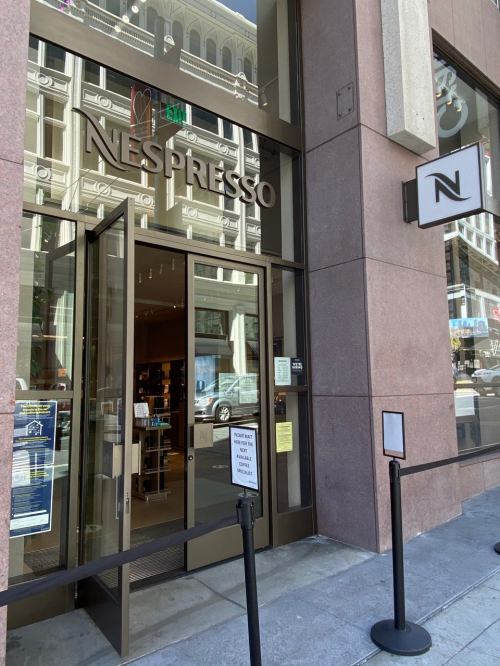 Entrance of a Nespresso store with glass doors and a modern facade, located in a city setting.