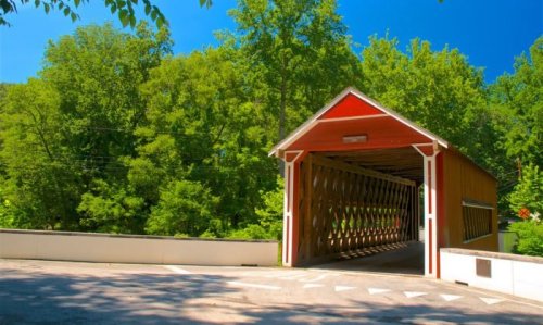 A red covered bridge surrounded by lush green trees under a clear blue sky.