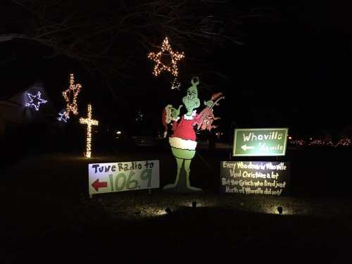 A festive display featuring the Grinch, Christmas lights, and signs promoting a radio station and Whoville theme.