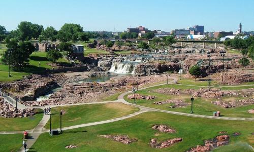 A scenic view of a waterfall surrounded by rocky terrain and green parks under a clear blue sky.