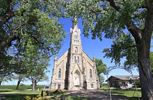A historic stone church framed by trees, with a clear blue sky in the background.