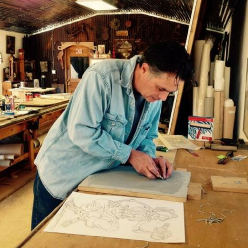 A person working on a creative project at a wooden table in a workshop, surrounded by art supplies and tools.