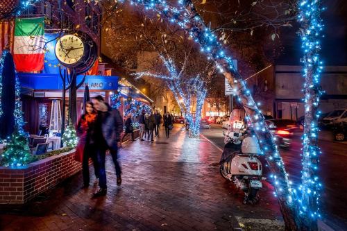 A festive street scene with blue lights, people walking, and decorated trees, creating a vibrant holiday atmosphere.