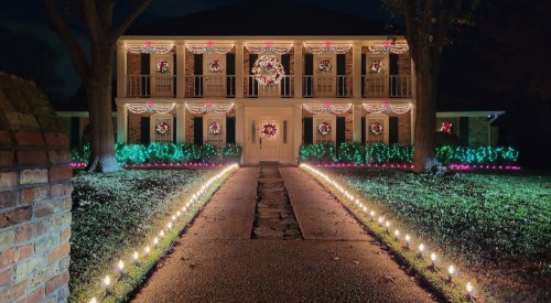 A beautifully decorated house at night, adorned with festive lights and wreaths along the walkway and porch.