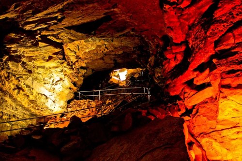 A dimly lit cave with colorful rock formations and a metal staircase leading upward.