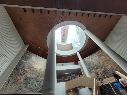 Interior view of a modern building featuring a circular skylight, tall columns, and large mural-covered walls.