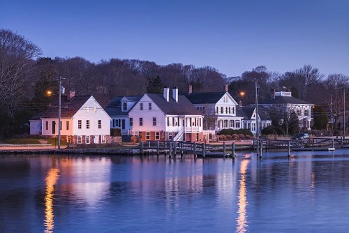 A serene waterfront scene at dusk, featuring charming houses reflecting in calm water.