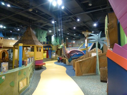 Colorful indoor play area with whimsical structures, including a castle, dragon, and palm trees, inviting children to explore.
