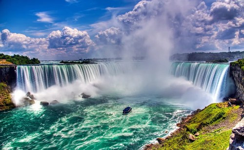 A stunning view of Niagara Falls with mist rising and a boat navigating the turquoise waters below.