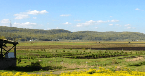 A scenic landscape featuring rolling hills, fields, and a clear blue sky with scattered clouds.