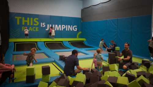 A vibrant indoor trampoline park with children jumping and playing on trampolines and foam blocks.