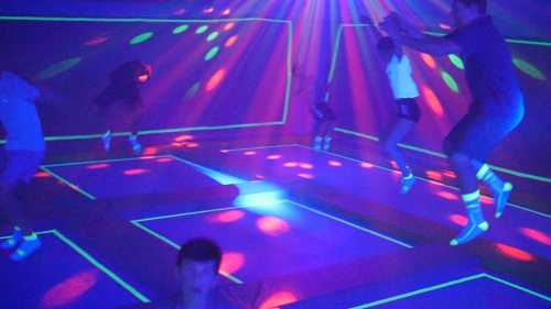 A group of children jumping in a brightly lit room with colorful lights and neon outlines on the floor.